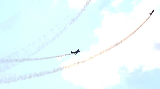 Aerobatic team propeller planes perform loops and vertical climbs leaving white smoke trails, blue sky with bright clouds, low angle telephoto shot