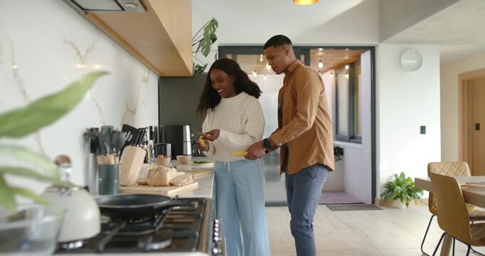African American couple laughing at kitchen counter, woman peeling banana after man reaching closer