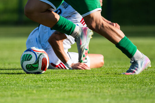 Soccer player falling on grass pitch duel with opponent for ball possession.
