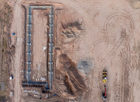 Aerial view of a construction site featuring a rectangular concrete foundation, piles of dirt, and heavy machinery including a loader and an excavator in Eagle, Colorado, United States.