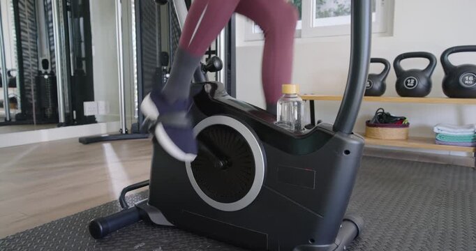 African American woman starting pedaling on elliptical in home gym for cardio, water bottle visible