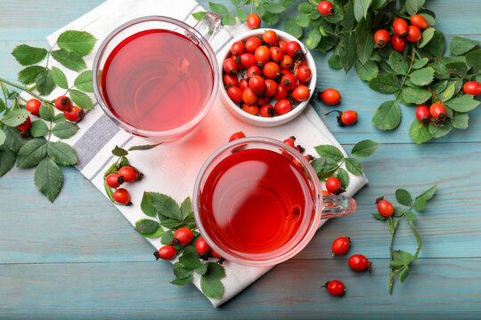 Aromatic rosehip tea in glass cups, berries and green leaves on light blue wooden table, flat lay