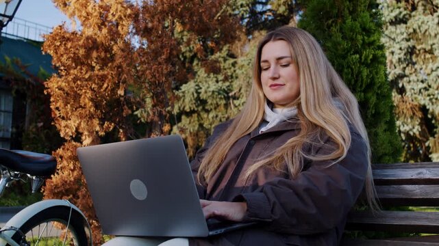 Woman author writes novel on laptop as rests in autumn park