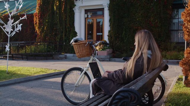 Lady types on laptop and bicycle parked nearby in autumn park