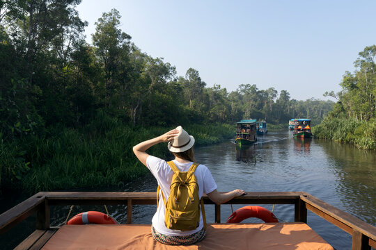 A large wooden boat took tourists to explore Tanjung Puting National Park in Kalimantan, Indonesia; a woman sits on the boat, enjoying the view.