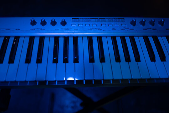 Synthesizer keyboard illuminated by blue stage light on dark concert background