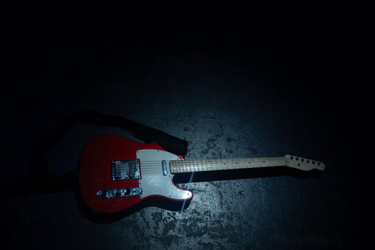 Red electric guitar lying on dark stage floor under spotlight