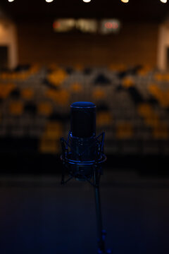Vertical close up of condenser microphone on stage with blurred auditorium background