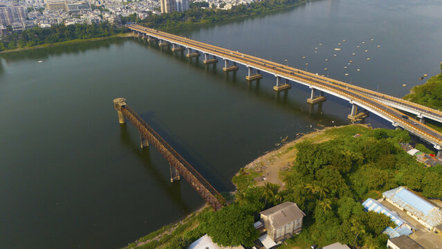 Aerial view of the bridges spanning the Tapi River with lush green trees along the riverbank and urban buildings in the background, Surat, Gujarat, India.