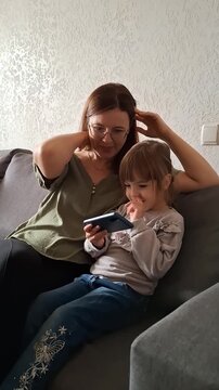 Mother and daughter spend time together while looking at a phone on the couch