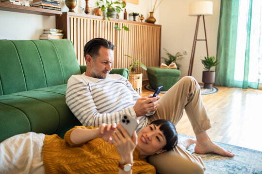 Couple lounging at home using smartphones on living room floor
