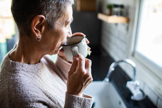 Senior woman sipping tea by the kitchen sink