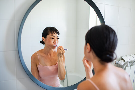 Woman brushing teeth in bathroom mirror