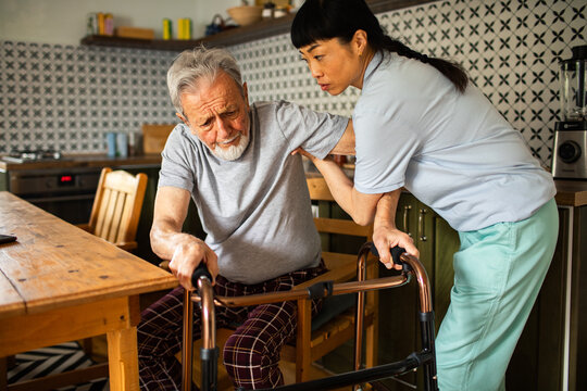 Caregiver helping senior man stand with walker in kitchen