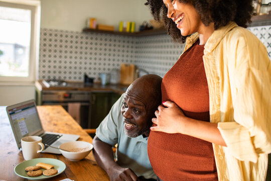 Man listening to pregnant partner's belly in kitchen