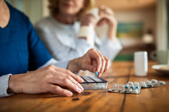 Caregiver sorting medication into pill organizer for senior woman