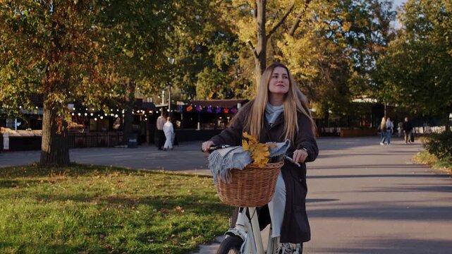Young female rides bicycle with wicker basket in autumn park