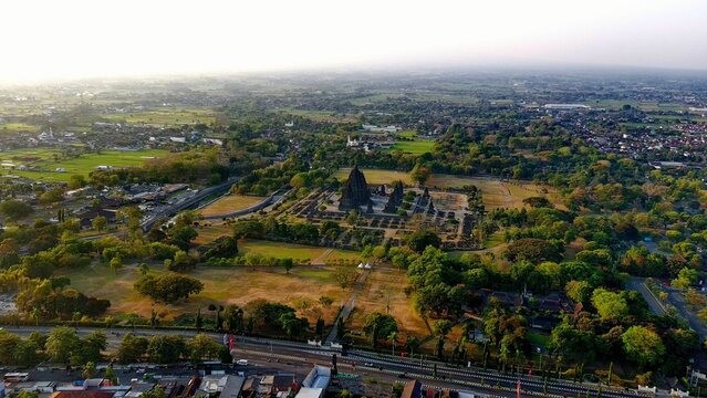Aerial view of the ancient Hindu Prambanan Temple complex surrounded by lush trees, expansive lawns, and the urban landscape of Prambanan, Special Region of Yogyakarta, Indonesia.
