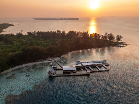 Aerial view of Karimun Jawa island with a wooden pier and fish farm structures in clear turquoise water at sunset, Karimunjawa, Central Java, Indonesia.