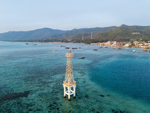 Aerial view of a metal navigational beacon in clear turquoise waters near Karimun Jawa island, with boats and a coastal village in the background Karimunjawa, Central Java, Indonesia.