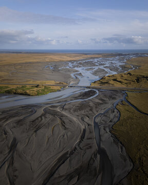 Aerial view of a braided river system flowing through a vast landscape with a bridge crossing the water towards the ocean in Iceland.