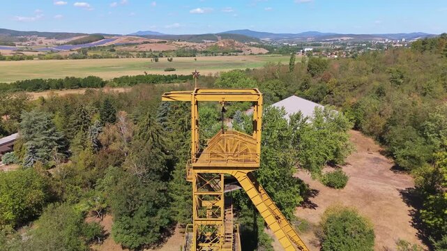 Aerial view of the historic Tiribesi-Akna coal mine headframe rising above trees and rural fields near B&aacute;tonyterenye, Hungary, in the N&oacute;gr&aacute;d coal basin during summer.