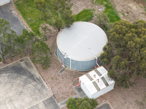 Melbourne, VIC, Australia - 14 October 2026: Aerial view of a large circular water tank and a small shed located within the Bayswater North industrial area, surrounded by trees and paved surfaces.