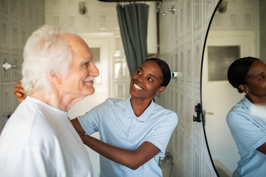 Caregiver helping senior man dress in bathroom