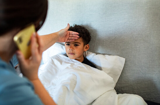 Caregiver checks sick boy's forehead while calling doctor
