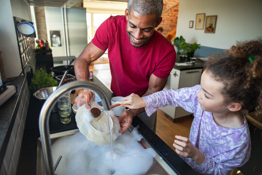 Man and child washing a colander at the kitchen sink