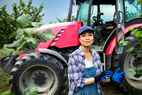 Woman farmer putting on gloves by red tractor