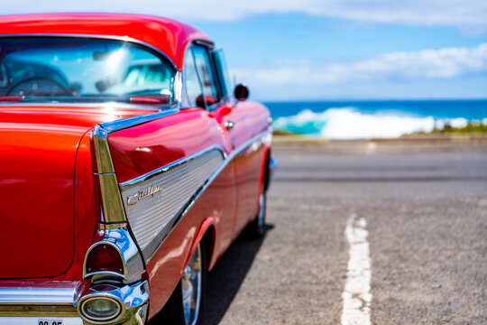 Honolulu, Hawaii, USA, 09 August 2025: Red 1957 Chevrolet Bel Air tailfin and badge with ocean waves at Sandy Beach Classic Car Meet.
