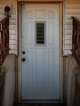 White exterior residential basement door framed by concrete side walls and rusted wrought iron railings