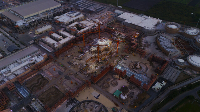 Surat, India - 08 October 2026: Aerial view of a large temple construction site with multiple cranes, stone structures, and expansive grounds under a dim evening sky.