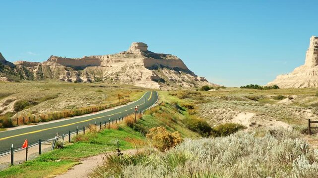Road view of asphalt highway winding toward towering sandstone bluffs at Scotts Bluff National Monument in Gering, Scotts Bluff County, Nebraska