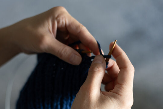 Close-up of woman hands knitting blue woolen fabric with circular needles at home