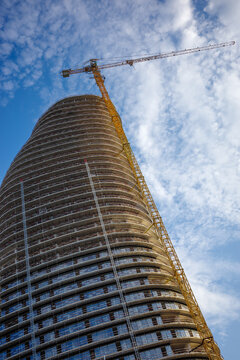 Skyscraper construction with tower crane beside curved high rise building, modern architecture under development with scaffolding, urban real estate expansion and construction engineering.