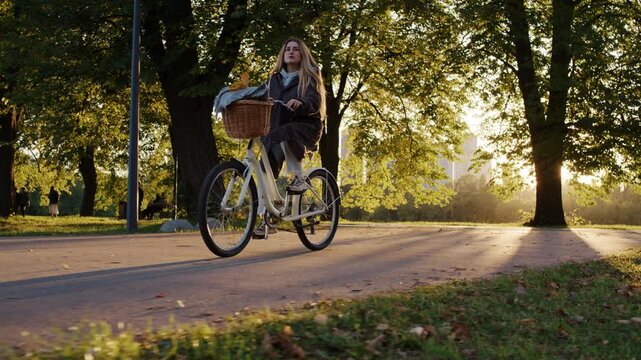 Autumn colors fill park as woman rides bicycle along paved path