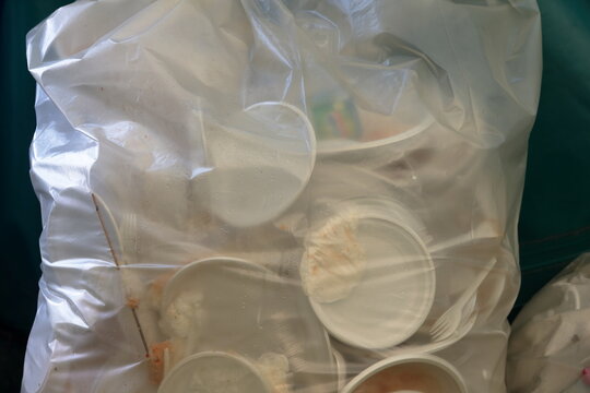Used disposable plastic plates and cutlery gathered inside a clear garbage bag ready for disposal