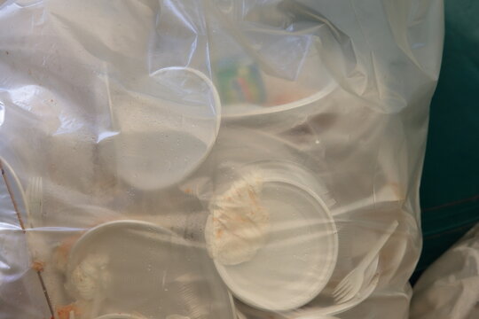 Used disposable plastic plates and cutlery gathered inside a clear garbage bag ready for disposal