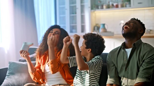 Excited family celebrating game win. Mom dad son high five sofa living room.