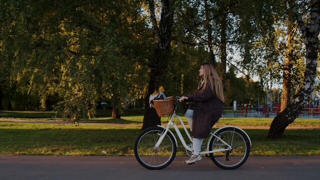 Female bicyclist in stylish outfit rides through autumn park