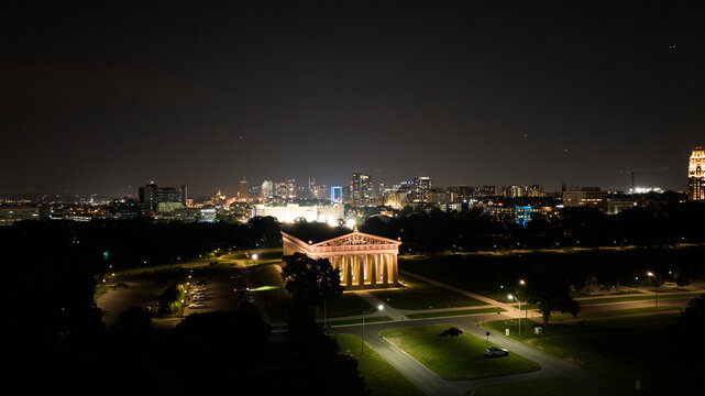 Nashville, Tennessee, United States - 24 May 2023: Aerial view of the illuminated Parthenon in Centennial Park at night with the Nashville city skyline glowing in the background.