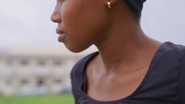 Close up portrait profile shows right half of woman face and neck. Woman wears dark top gold hoop earring with soft lighting against outdoor background