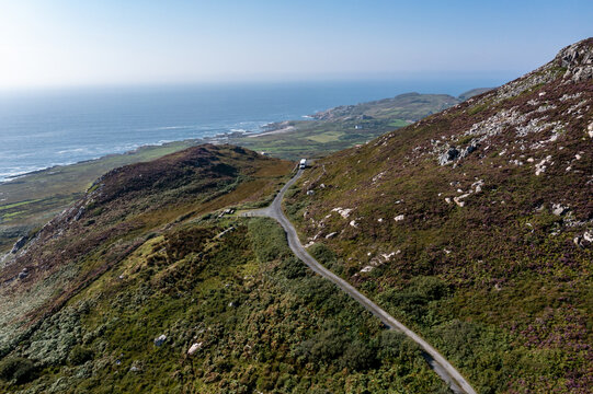 Maghery, County Donegal, Ireland - 10 October 2026: Aerial view of a DPD delivery van on a narrow coastal road winding through rugged, heather-covered hills with the Atlantic Ocean.