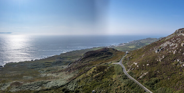 Maghery, County Donegal, Ireland - 10 October 2026: Aerial view of a DPD delivery van on a narrow coastal road winding through rugged, heather-covered hills by the Atlantic ocean.