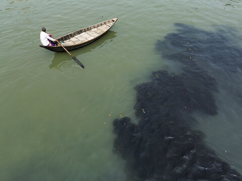 Dhaka, Bangladesh - 07 October 2026: Aerial view of a lone fisherman rowing a wooden boat across a river with a large patch of dark polluted water.