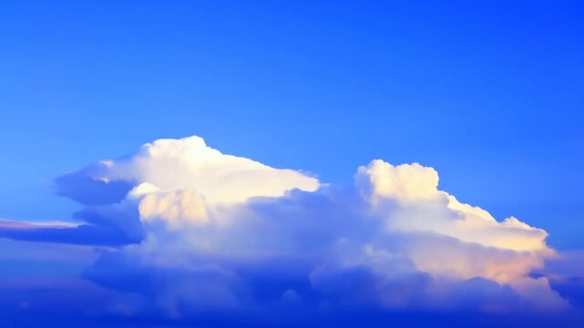 Towering cumulonimbus clouds rise and grow across a blue sky in warm sunlight