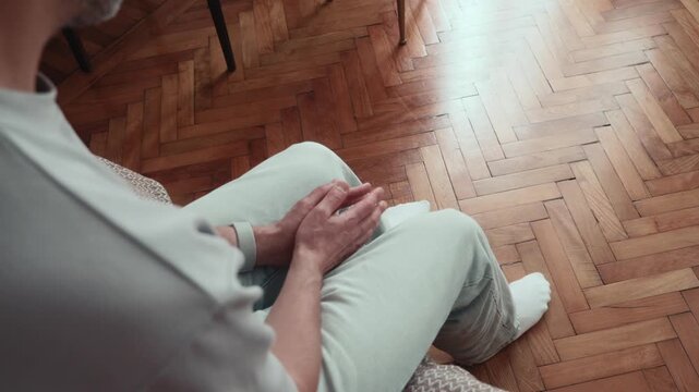 Man nervously fidgeting with hands and moving legs while sitting on bed, repetitive finger movements and restless body language expressing anxiety and inner tension.