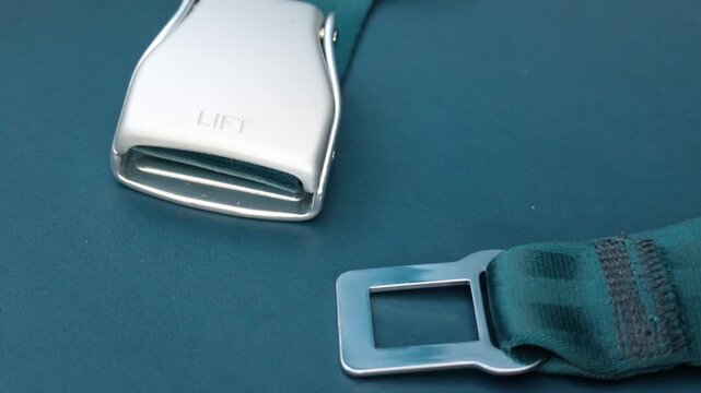 Airplane seat belt buckle and metal latch unfastened on blue passenger seat cushion